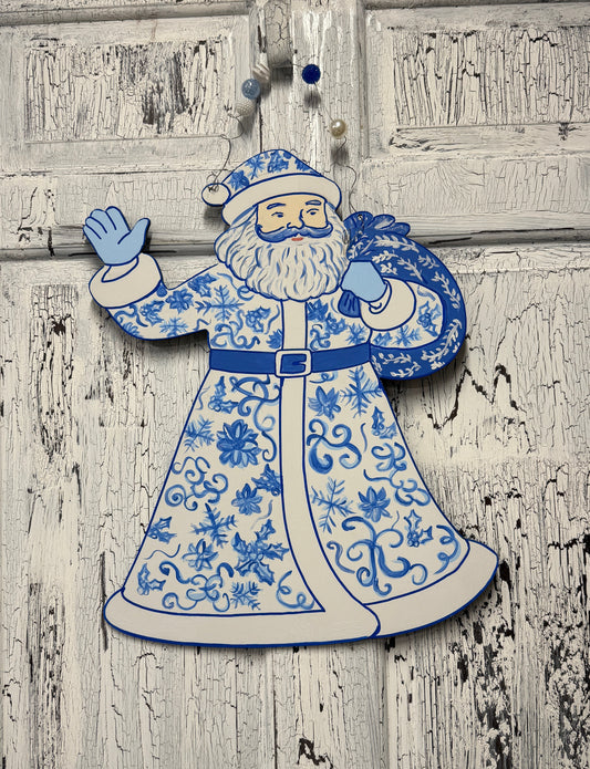 Decorative figure of a traditional Santa Claus in blue and white attire on a wooden background.
